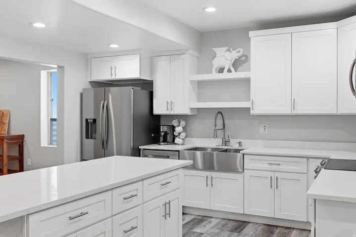 Modern kitchen featuring white shaker cabinetry, stainless steel appliances, a large center island with a light-toned countertop, and wood-finish flooring