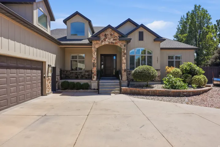 Stone archway entry with a dark wood front door, multi-pane arched window, an attached two-car garage, dormer windows, and a landscaped front yard with a retaining wall