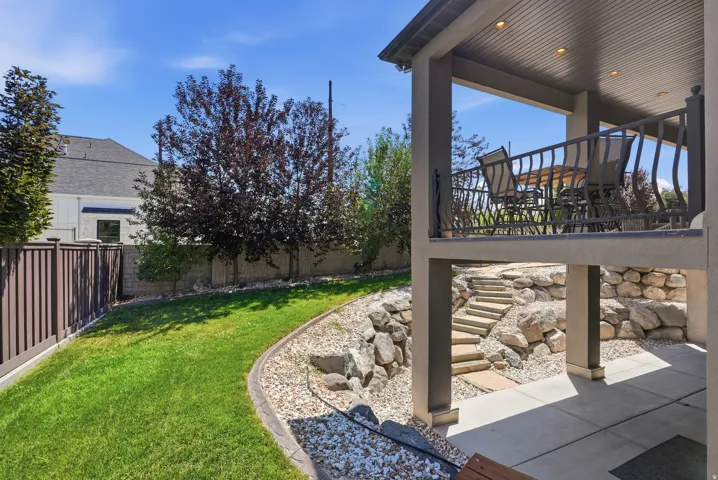 Multi-level outdoor living space featuring a covered lower patio with concrete flooring, stone steps, and an upper balcony with decorative metal railing