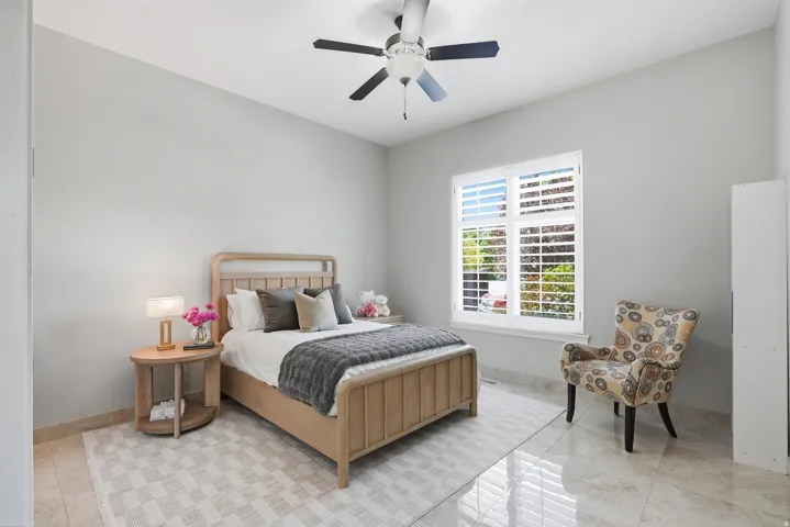 Spacious room featuring tile flooring, a large window with white plantation shutters, and a ceiling fan with integrated lighting