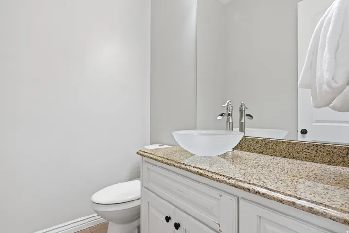 Bathroom featuring a white vanity with black hardware, a granite-finish countertop, and a vessel sink with a brushed nickel faucet