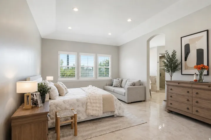 Spacious room featuring tray ceilings, recessed lighting, polished flooring, plantation shutters, and an arched doorway