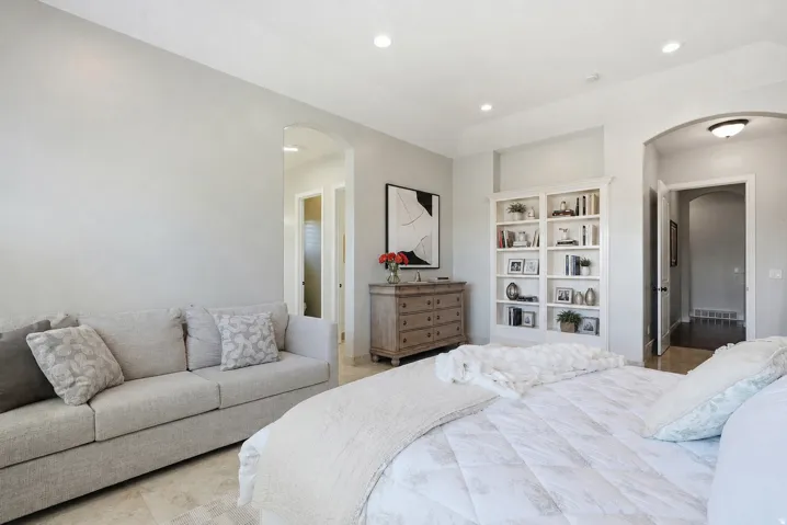 Recessed ceiling lighting illuminates a spacious room featuring light-toned flooring, an arched doorway, and built-in shelving