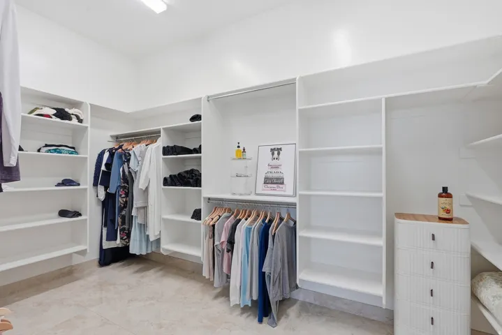 Spacious walk-in closet featuring extensive built-in shelving, multiple hanging rods, recessed ceiling lighting, and light-toned tile flooring