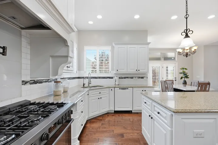 Kitchen featuring white cabinetry, granite countertops, stainless steel appliances, wood-finish flooring, and a decorative tile backsplash