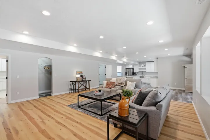 Open-concept living area featuring wood-finish flooring, recessed lighting, an arched entryway, and a full kitchen with white cabinetry and stainless-steel appliances