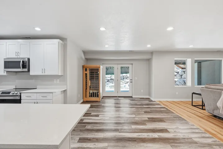 Open-concept living space with wood-finish flooring, recessed lighting, and kitchen area featuring white cabinetry, light-toned countertops, and stainless steel appliances