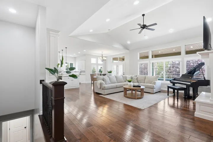 Open-concept living space featuring wood-finish flooring, vaulted ceilings with recessed lighting, and a ceiling fan