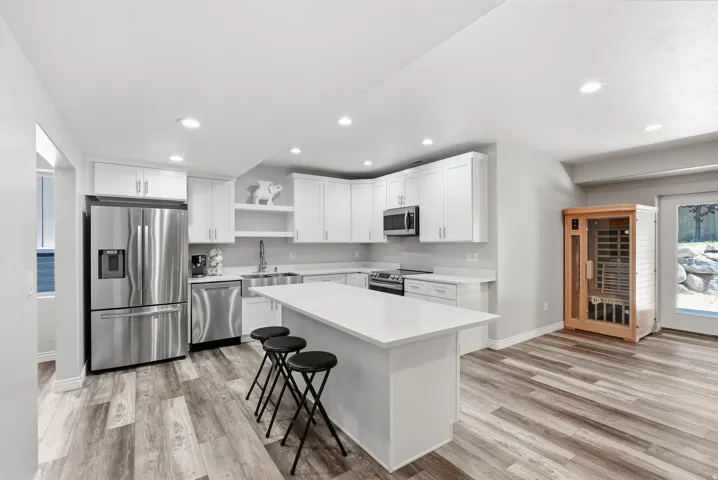 Modern kitchen featuring white cabinetry, stainless steel appliances, a white island with countertop seating, recessed lighting, and wood-finish flooring