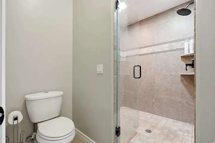 Glass-enclosed shower with tiled walls and floor, featuring a rainfall showerhead and built-in shelving