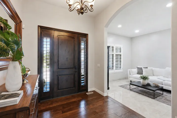 Grand entry with wood-finish flooring and a decorative chandelier, featuring a dark wood front door with sidelight windows