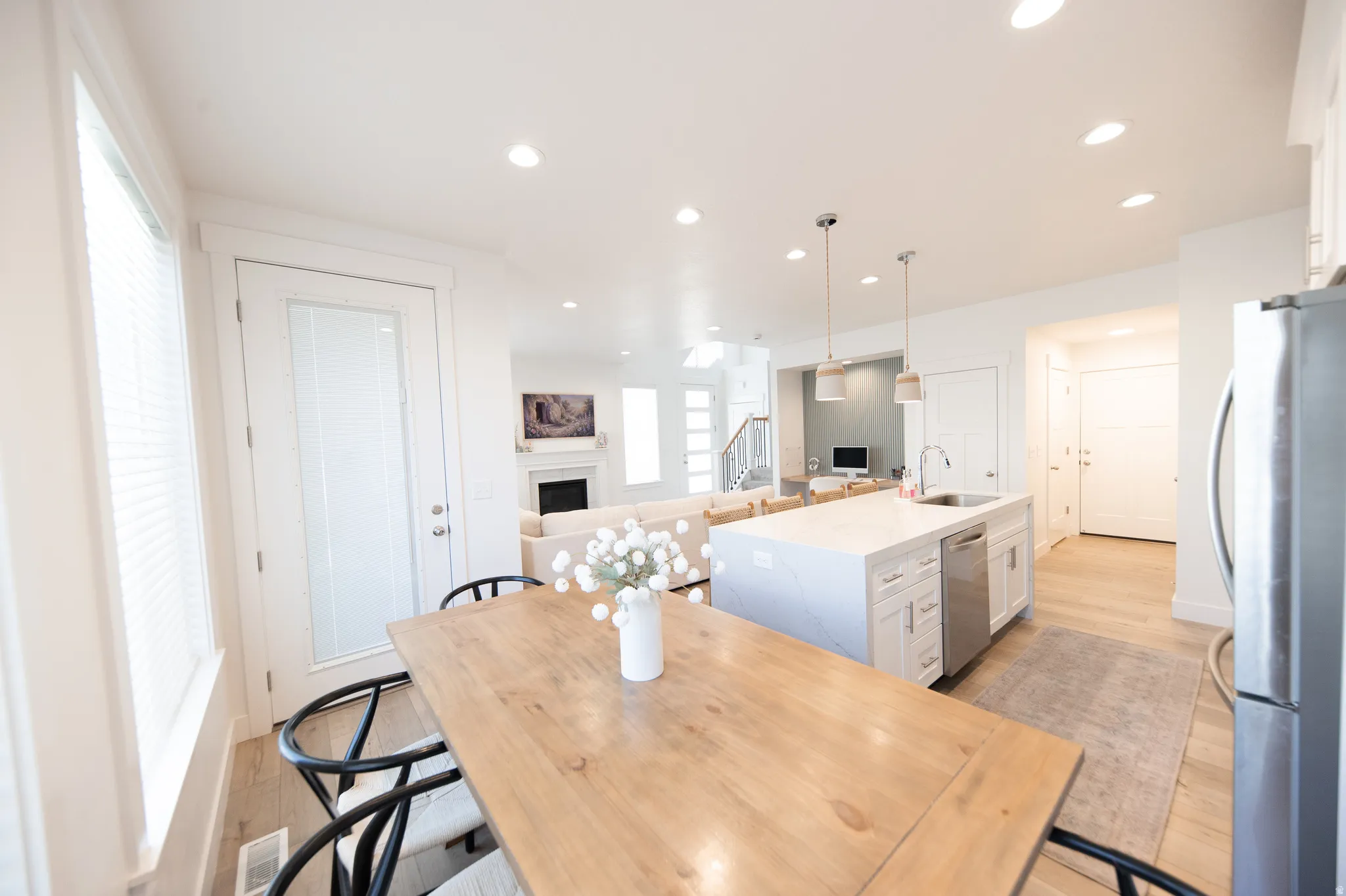 Open-concept kitchen and dining area featuring a light-toned wood dining table, white kitchen island with an undermount sink, stainless steel dishwasher, and recessed lighting throughout