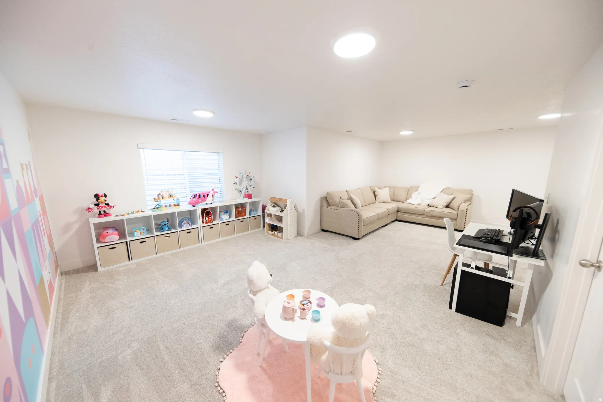 Spacious room featuring light-colored carpeting, multiple circular ceiling lights, a large window with blinds, and white walls