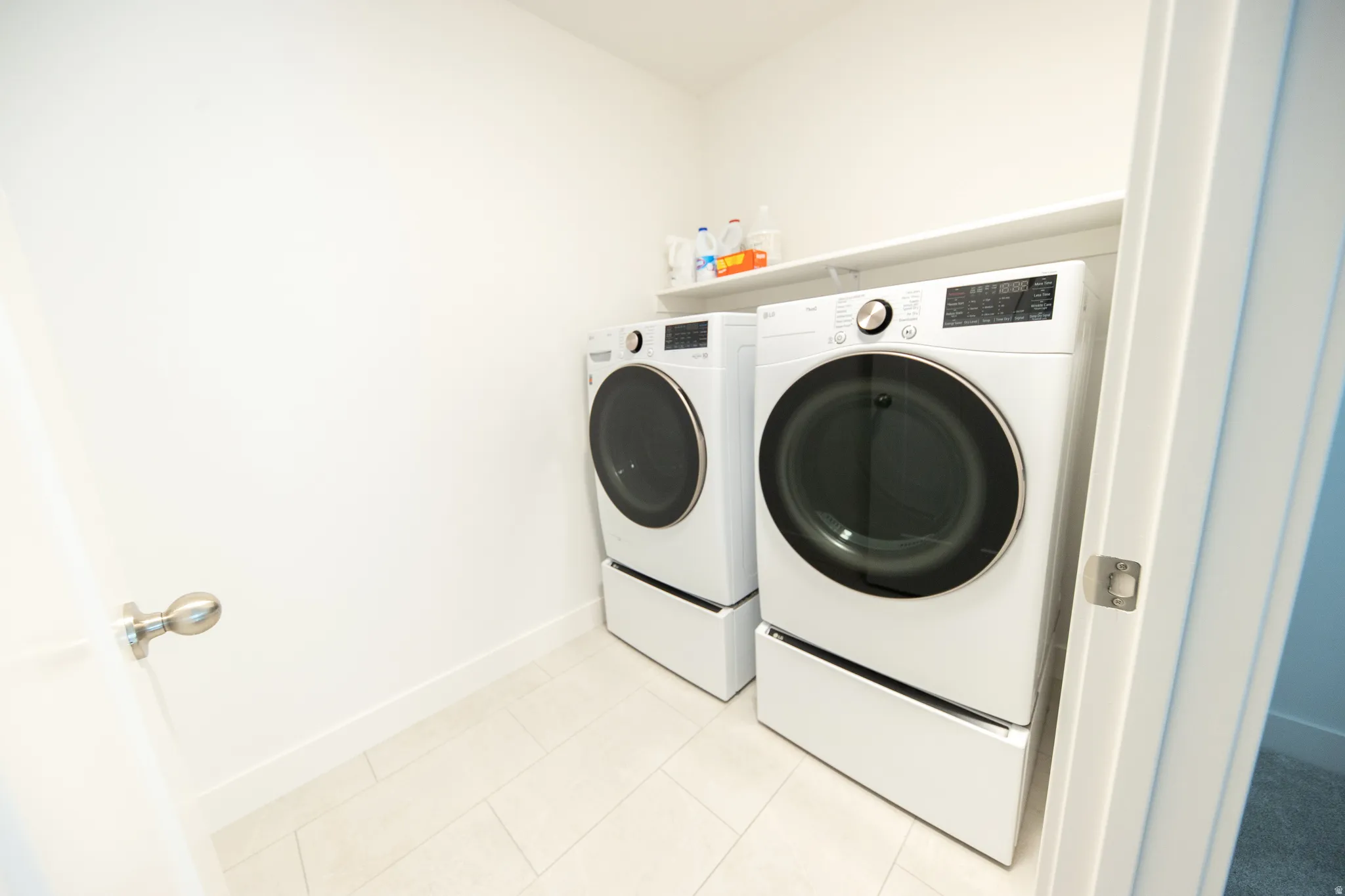 Laundry area featuring light-toned tile flooring and a built-in storage shelf