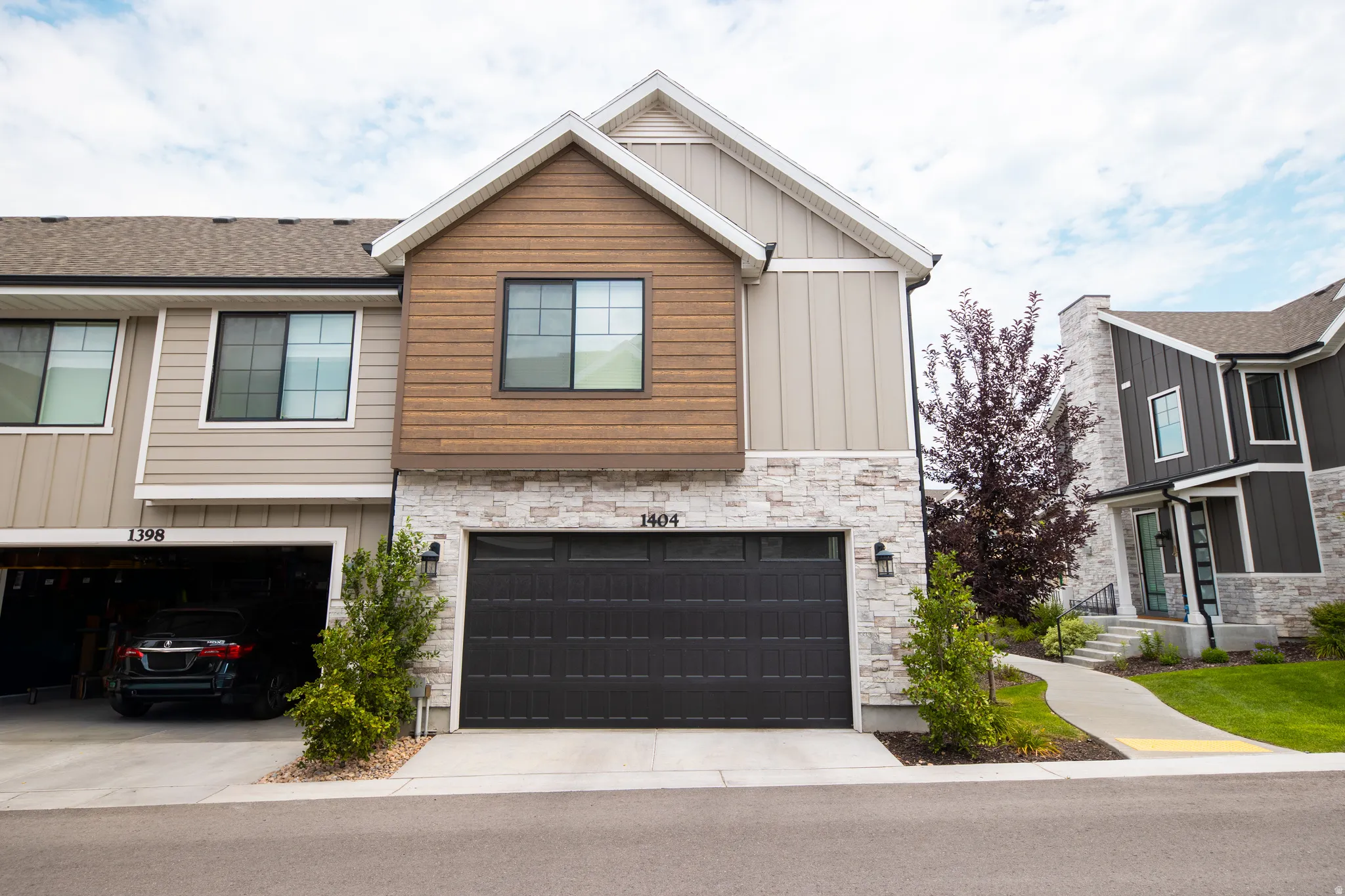Modern townhome exterior featuring a two-car garage with a dark panel door, a stone facade, and horizontal wood-finish siding accents