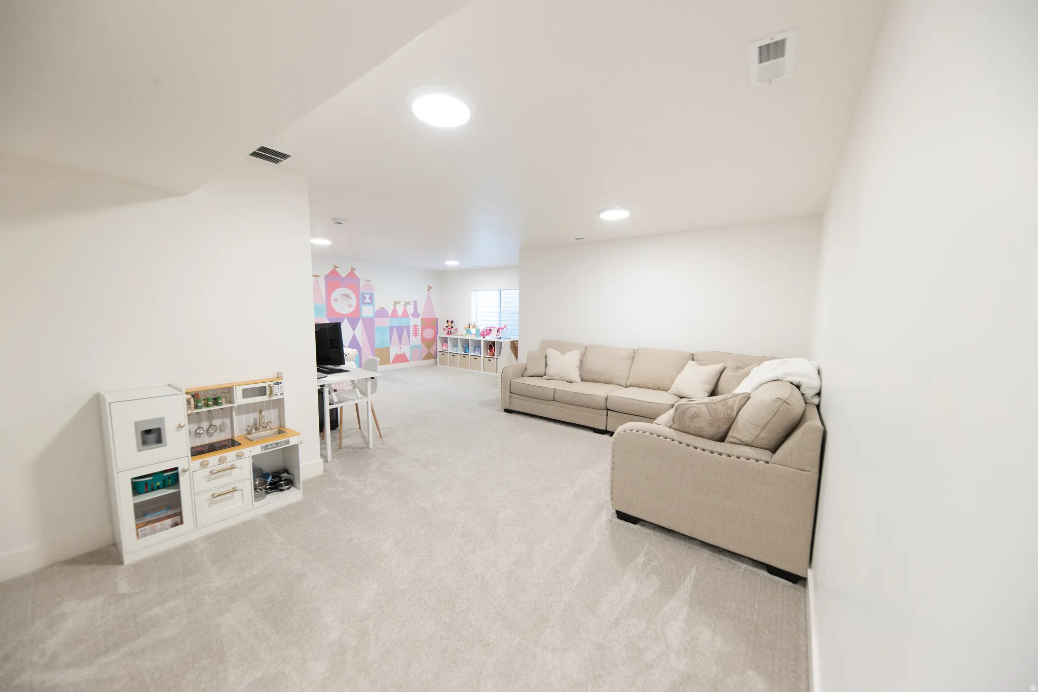Expansive recreational space featuring light gray carpeting, recessed ceiling lighting, and a white wall finish