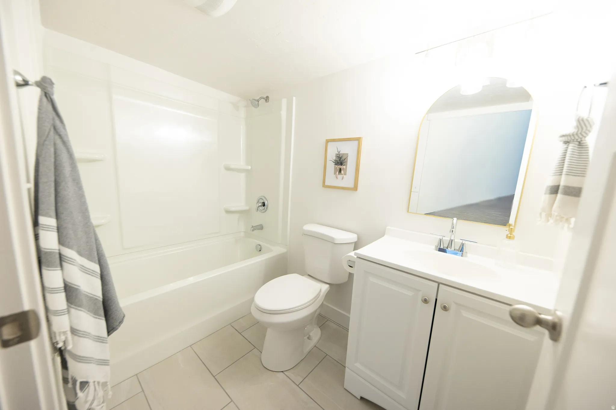 Bathroom featuring a white bathtub and shower surround, white vanity with integrated sink, chrome faucet, and a wall-mounted arched mirror