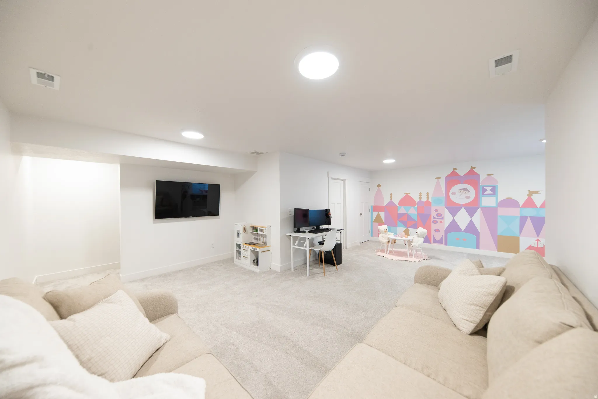 Spacious carpeted room featuring recessed lighting, a mounted television, a colorful wall mural, and a white door with contemporary hardware