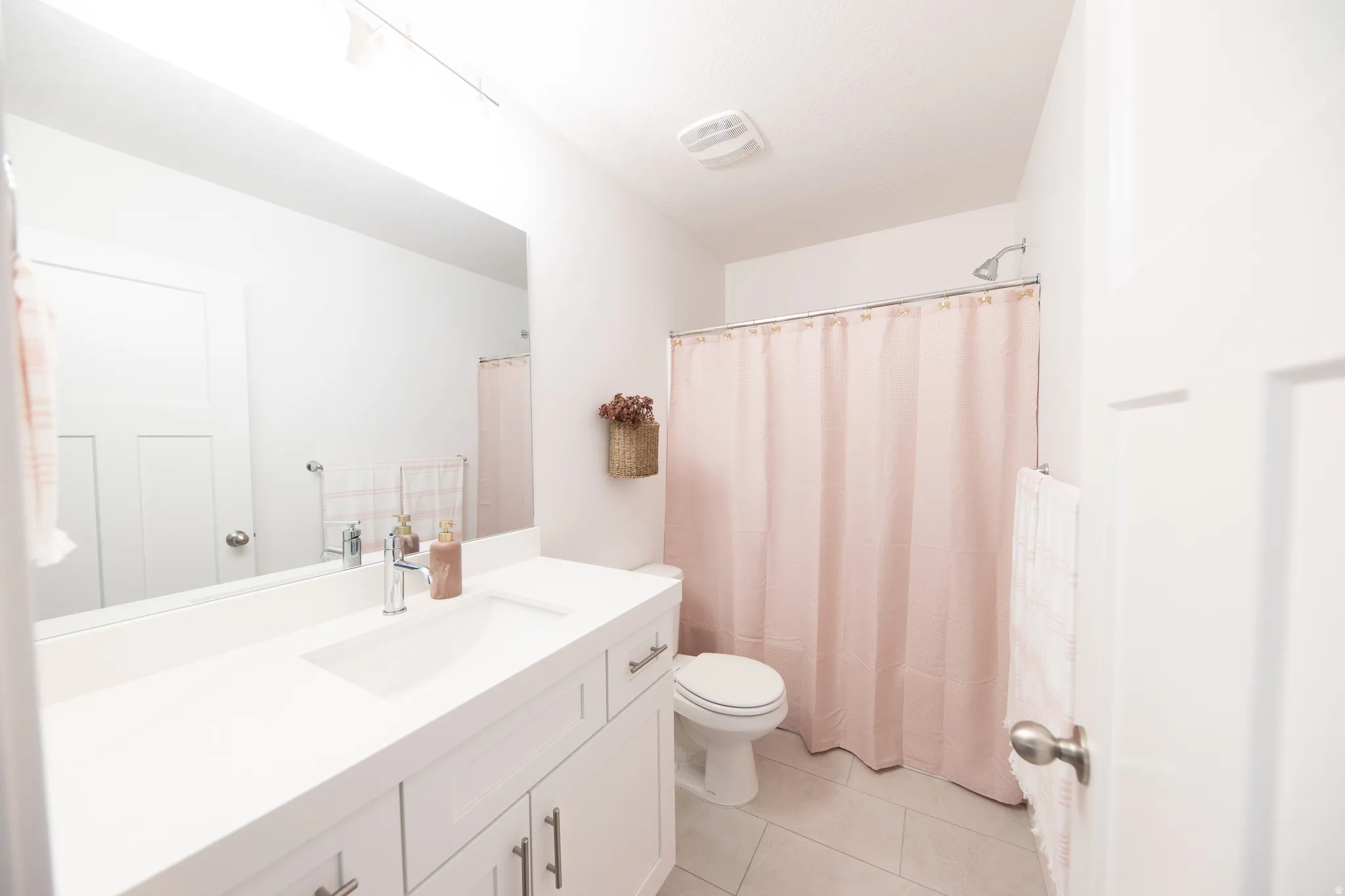 Bathroom featuring a single vanity with an integrated sink, white cabinetry with brushed nickel hardware, a rectangular mirror, and light-toned floor tiles