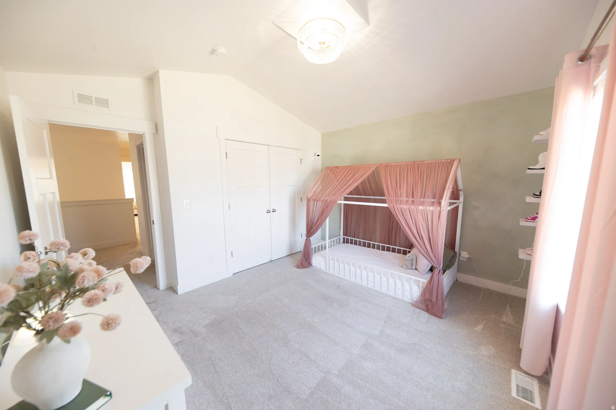 Spacious room featuring vaulted ceilings, light gray carpeting, a built-in closet with double doors, and a decorative accent wall