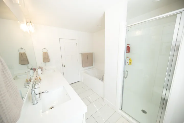 Bright bathroom with dual vanity, integrated sinks, chrome fixtures, and a spacious glass-enclosed shower