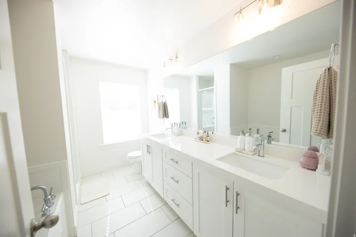White bathroom featuring a dual vanity with undermount sinks, a large mirror, and overhead lighting