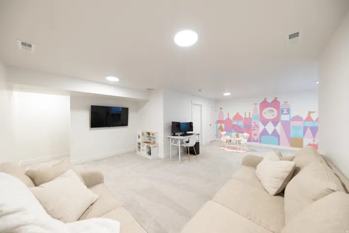 Spacious carpeted room featuring recessed lighting, a mounted television, a colorful wall mural, and a white door with contemporary hardware