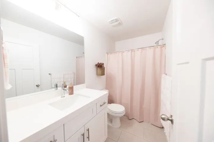 Bathroom featuring a single vanity with an integrated sink, white cabinetry with brushed nickel hardware, a rectangular mirror, and light-toned floor tiles