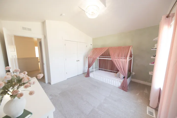 Spacious room featuring vaulted ceilings, light gray carpeting, a built-in closet with double doors, and a decorative accent wall