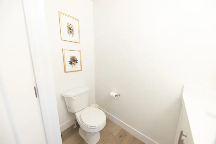 Powder room with light wood-finish flooring, white walls, and a white vanity with a white countertop