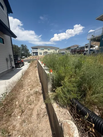 Developing property lot featuring a concrete retaining wall, a side yard with gravel, and a corrugated drainage pipe