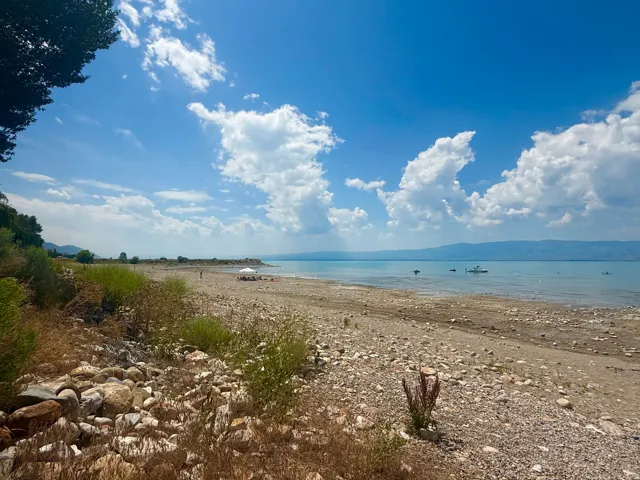 Rocky shoreline with calm, clear water under a wide blue sky