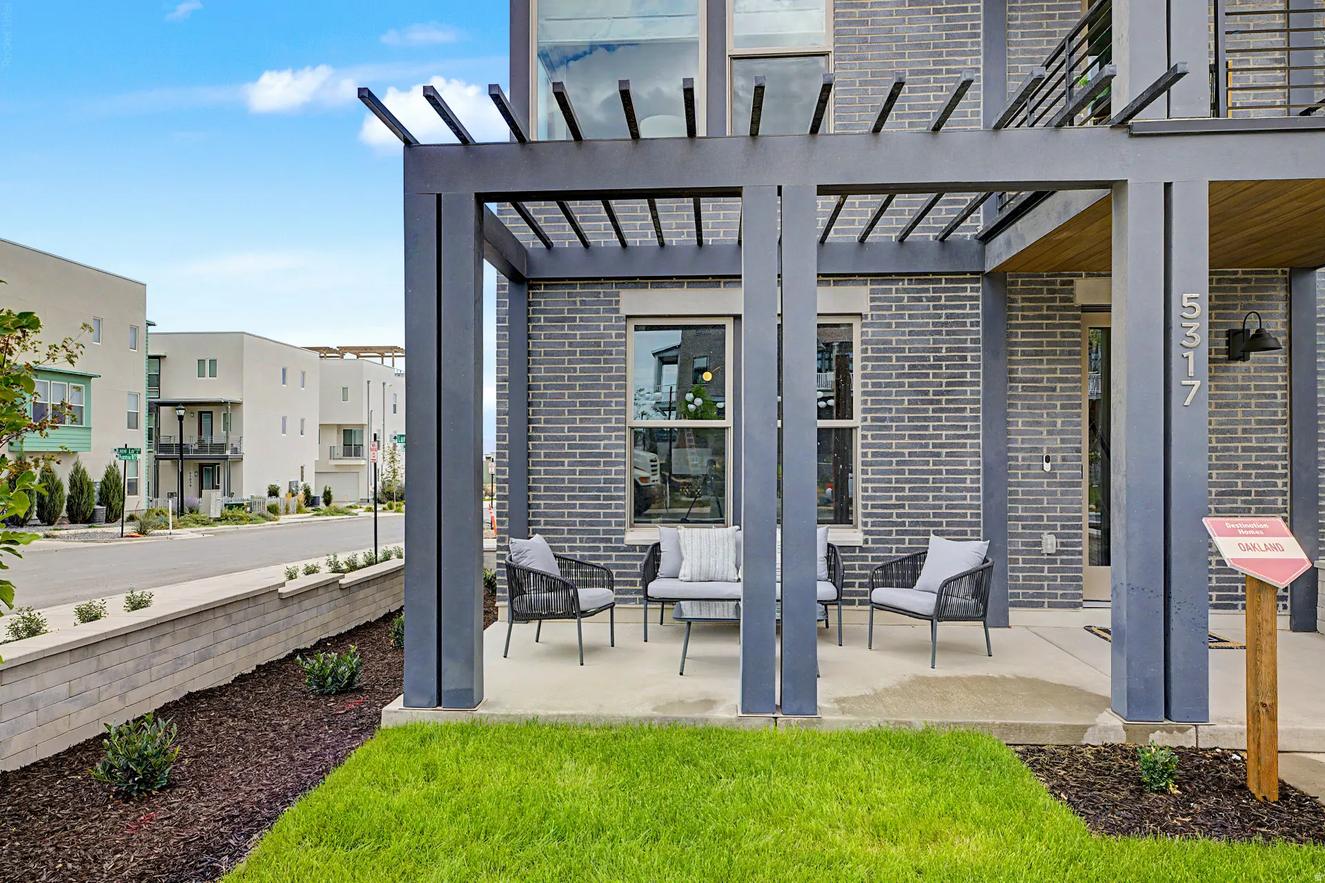 Paved patio with a dark grey pergola, brick facade, and street-facing windows