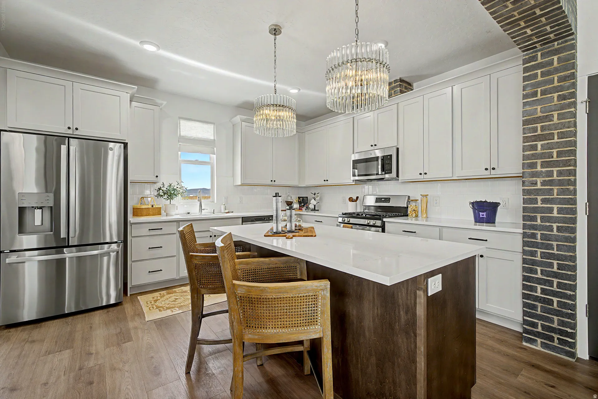 Modern kitchen featuring white shaker cabinetry, stainless steel appliances, a center island with a white countertop, wood-finish flooring, and two decorative pendant lights