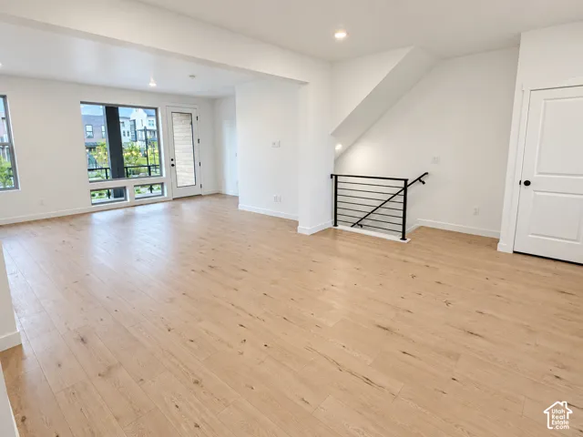 Spacious interior with light wood-finish flooring, recessed lighting, and a modern black metal staircase railing