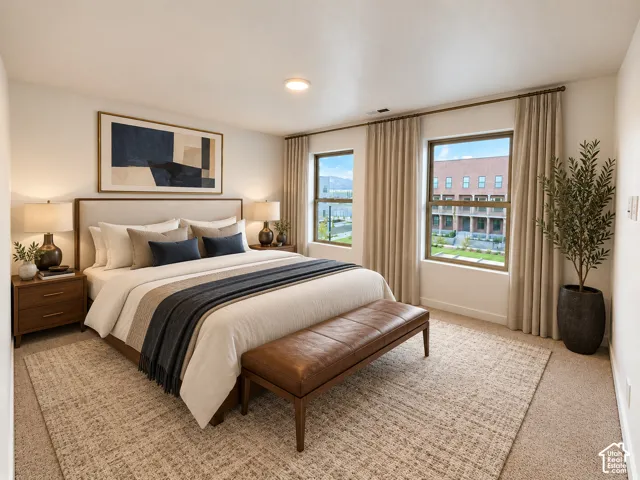 Spacious room featuring neutral carpet flooring, a light-colored upholstered headboard, and two large windows