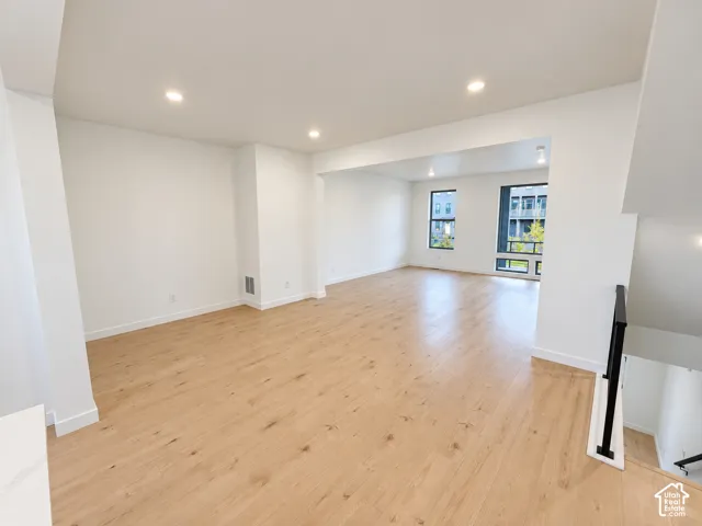 Recessed lighting, wood-finish flooring, white walls, black window frames, and a black metal stair railing