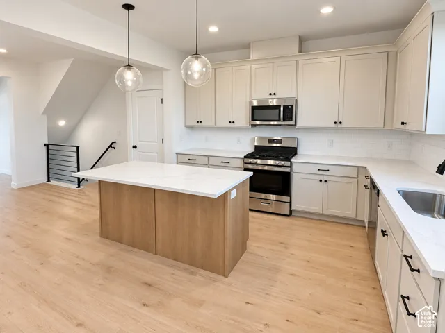 Kitchen featuring light wood-finish flooring, a central island with a white countertop, white shaker-style cabinetry, and stainless steel appliances