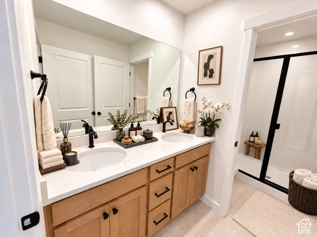 Dual undermount sinks, light wood-finish cabinetry, white countertop, large wall-mounted mirror, and a glass-enclosed shower with black trim