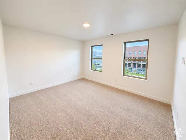Recessed ceiling light, neutral tone carpeting, and two windows with dark frames
