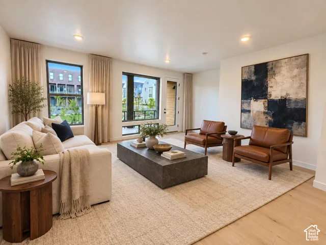 Recessed lighting, light wood-finish flooring, large windows, white walls, and a glass-paneled door