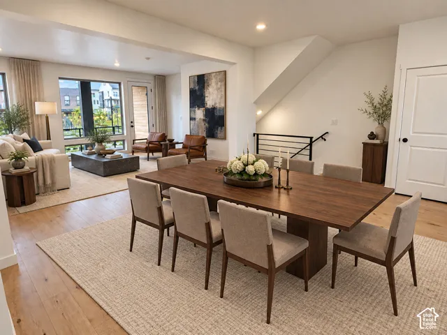 Open-concept living area featuring wood-finish flooring, recessed lighting, expansive windows, and a contemporary staircase with a black metal railing