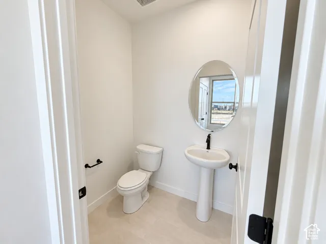 Pedestal sink with a matte black faucet, oval mirror, and tile flooring