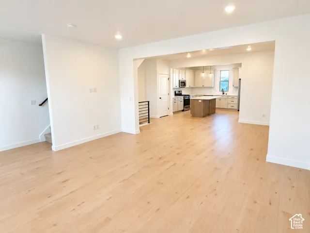 Open-concept living area featuring light wood-finish flooring, recessed lighting, and a modern kitchen with a large island and pendant lighting