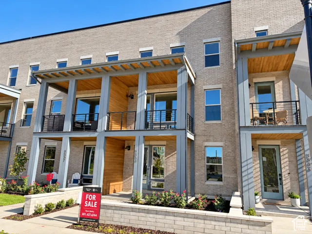 Contemporary multi-story facade featuring light-toned brick, multiple balconies with black railings, and wood-finish ceiling accents