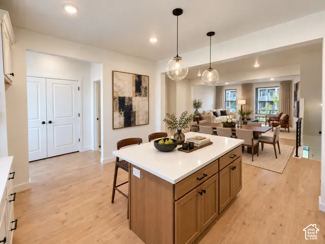 Central kitchen island with a light-toned countertop, wood-finish flooring, recessed lighting, double-door entryway, and suspended pendant lighting fixtures