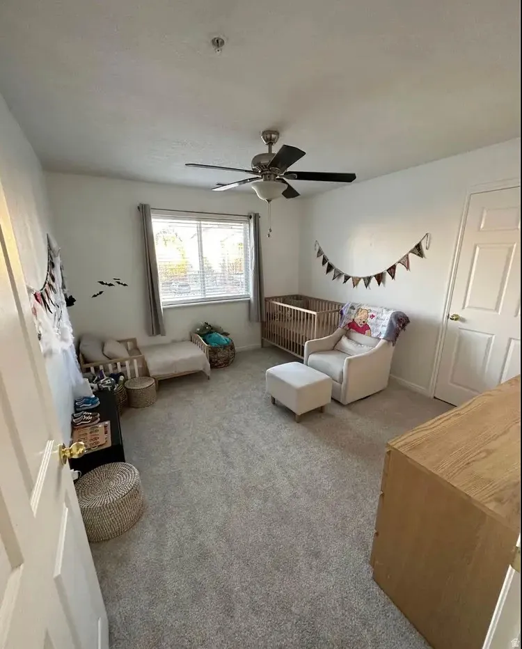 Carpeted room featuring a ceiling fan with integrated lighting, a double-hung window with blinds and drapes, and a white paneled door