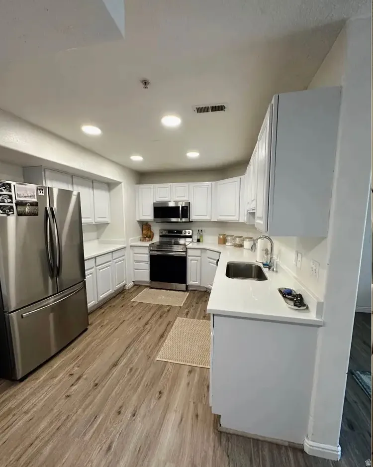 Modern kitchen featuring white cabinetry, light countertops, wood-finish flooring, stainless steel appliances, and recessed lighting