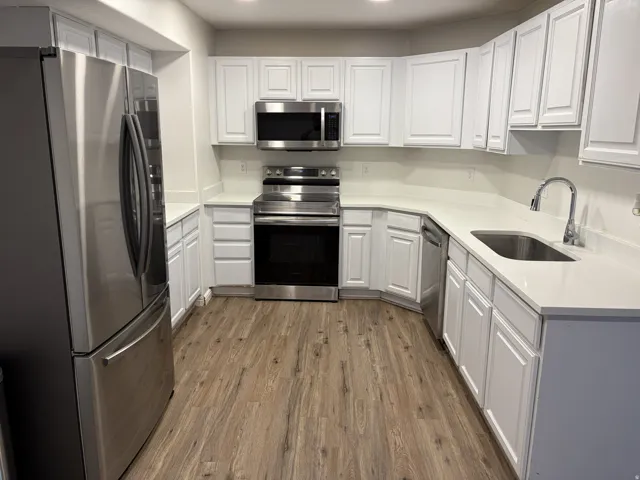 Kitchen featuring white cabinetry, stainless steel appliances, white countertops, and wood-finish flooring