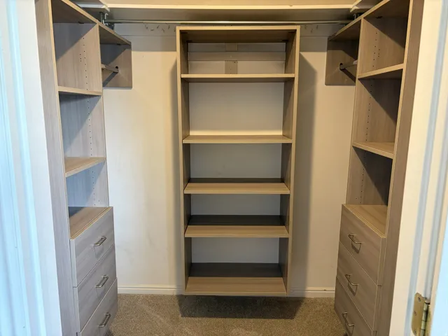 Custom closet system featuring light wood-finish shelving, built-in drawers with modern pulls, and hanging rods for garment storage